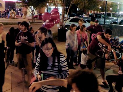 Several people walking by physics demonstrations at First Friday in Downtown, Bryan.