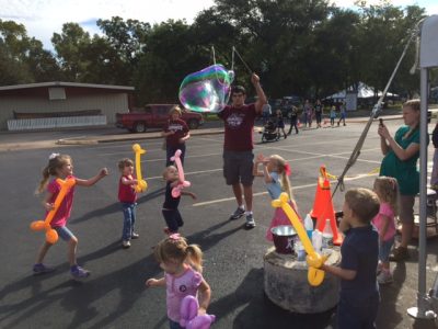 A student making giant bubbles near children.