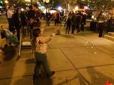 A girl chasing bubbles in the sidewalk.